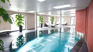 An indoor swimming pool with clear water, surrounded by lounge chairs and potted plants. - Hotel Freihof (Prichsenstadt)
