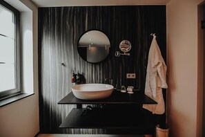 A modern bathroom with a large oval sink, a round mirror, and a towel rack. - Hotel Freihof (Prichsenstadt)
