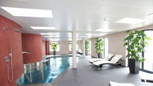 An indoor swimming pool with lounge chairs and potted plants. - Hotel Freihof (Prichsenstadt)