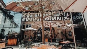 An outdoor dining area with wooden tables and chairs, surrounded by umbrellas and a tree. - Hotel Freihof (Prichsenstadt)