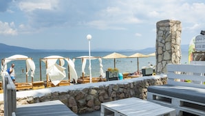 A beachside lounge with wooden furniture, white canopies, and a stone wall.