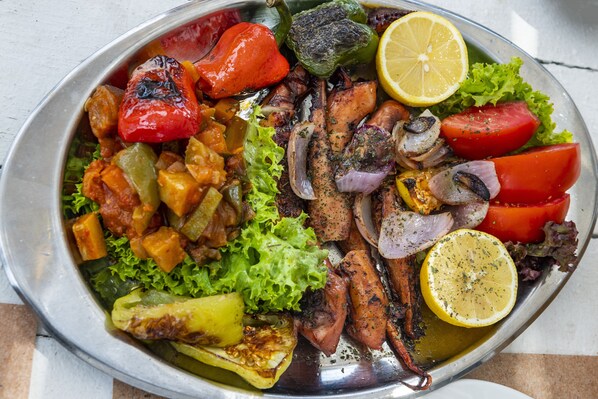 Une assiette de légumes et de viandes grillés, notamment des tomates, des poivrons et des oignons, présentée sur un plateau en métal.