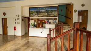 A hotel lobby with a reception desk, a staircase, and a view of the beach.