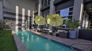 A swimming pool with two umbrellas, lounge chairs, and potted plants. - Fairfield Inn & Suites by Marriott Mexicali (Mexicali)