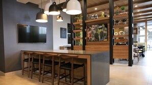 A modern kitchen with a bar area, wooden chairs, pendant lighting, and a large flat-screen TV. - Fairfield Inn & Suites by Marriott Mexicali (Mexicali)