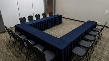 Un salón de conferencias con una larga mesa y sillas, piso alfombrado y paredes lisas.