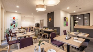 A modern dining area with multiple tables and chairs, a kitchen in the background, and decorative wall art. - Hotelmyhome (Hornberg)