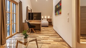A modern hotel room with a wooden floor, a desk with a chair, a bed, a TV, and a painting on the wall. - Hotelmyhome (Hornberg)