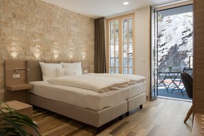 A modern bedroom with a large bed, a wooden headboard, a nightstand, and a view of a balcony with outdoor seating. - Hotelmyhome (Hornberg)