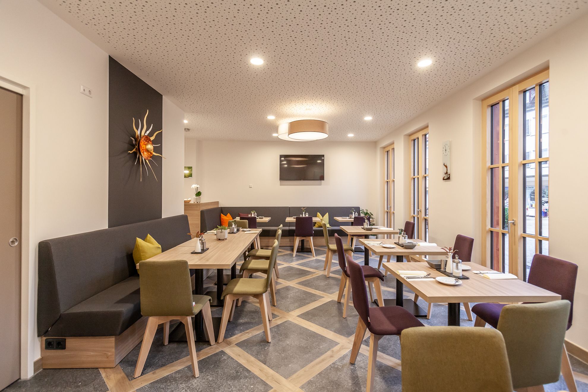 Et moderne spiseområde med forskellige siddepladser, herunder borde og en sofa, med et loft med et unikt mønster og indbygget belysning.