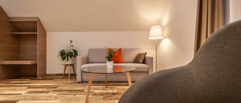Un salon moderne avec un canapé, une table basse en verre et un lampadaire. On y trouve également une étagère en bois et une plante en pot posée sur une petite table.