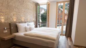 A bedroom with a large bed, a wooden nightstand, and a view of a balcony with a wooden railing. - Hotelmyhome (Hornberg)
