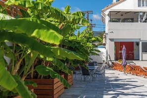A patio area with outdoor seating, a laptop on a table, and a building with a red door in the background.