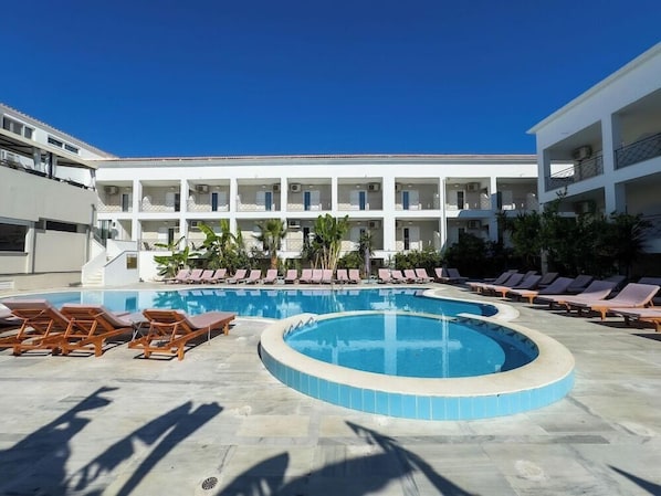 A pool area with lounge chairs and a building with balconies.