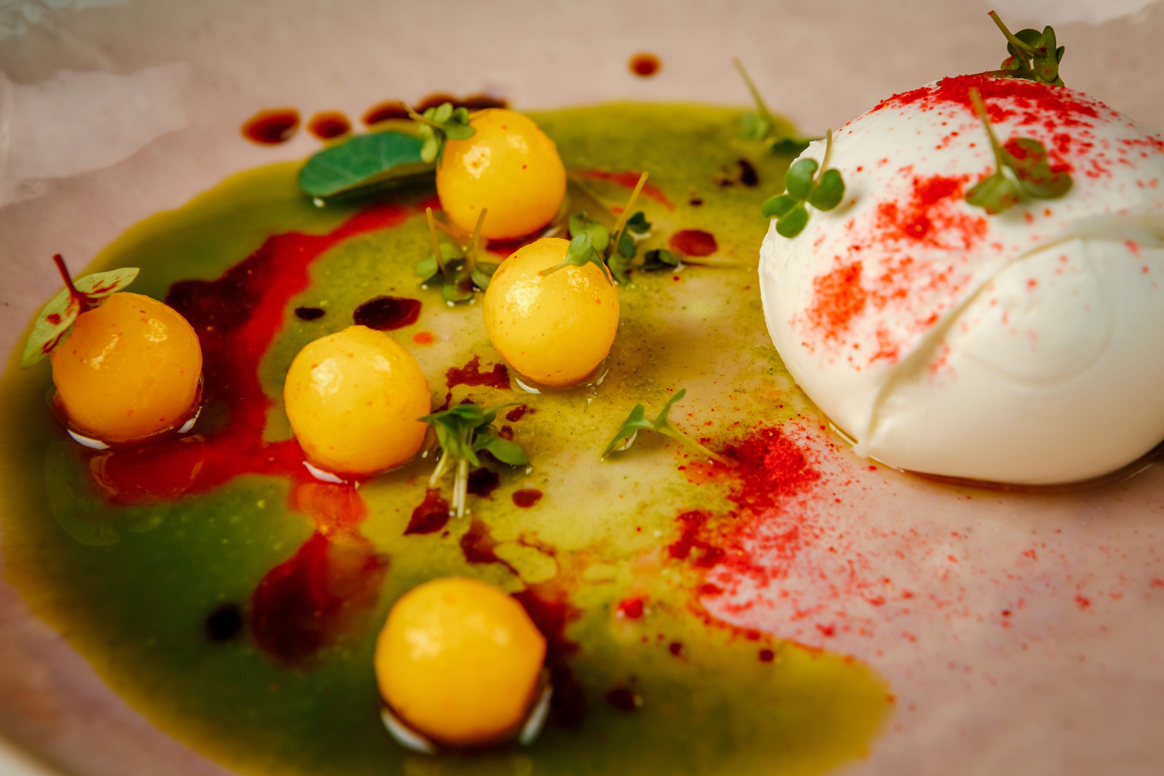 A dish with spherical yellow items, a white spherical item, and green leaves on a plate.