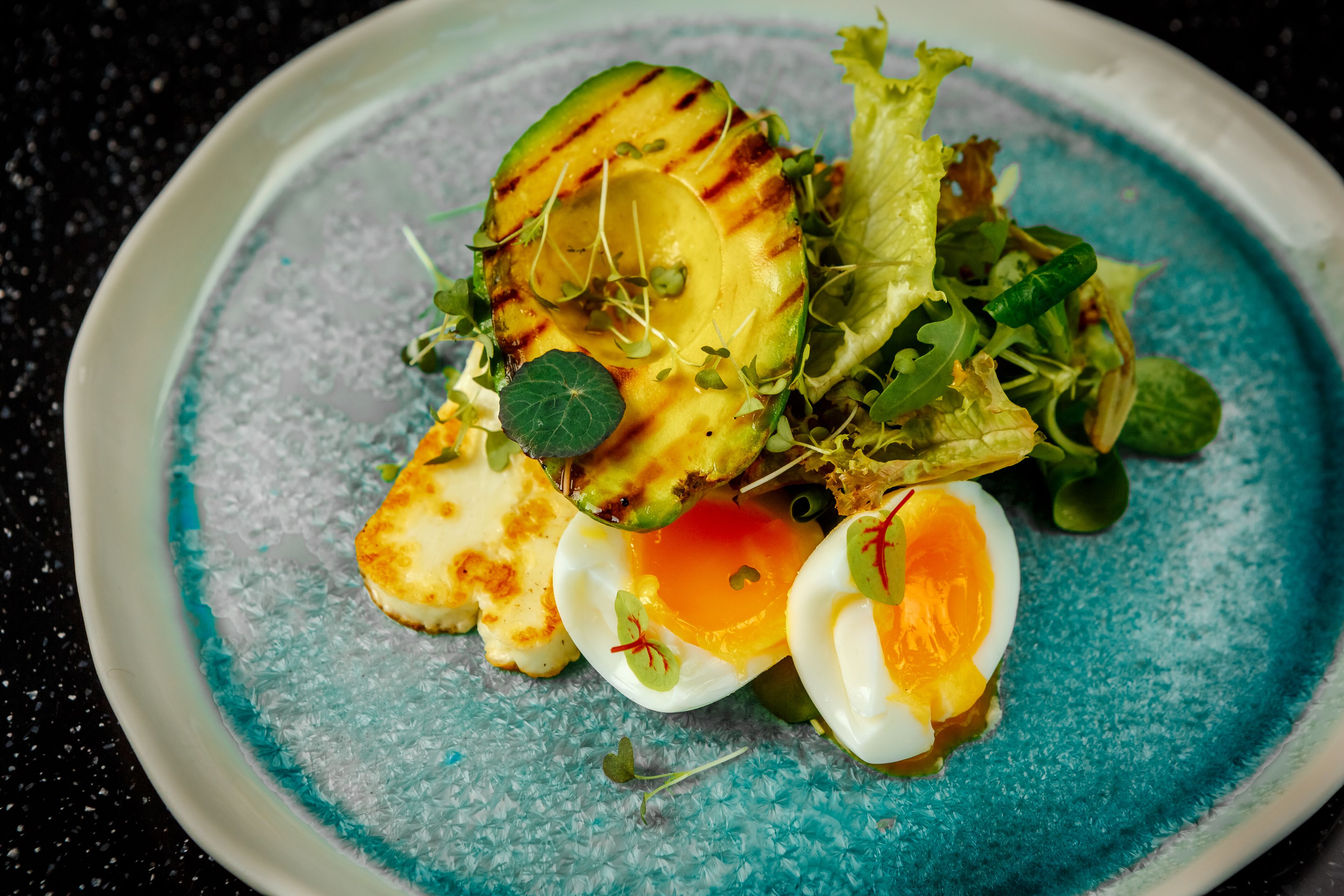 En tallrik med grillade grönsaker, sallad och ett halverat, kokt ägg.