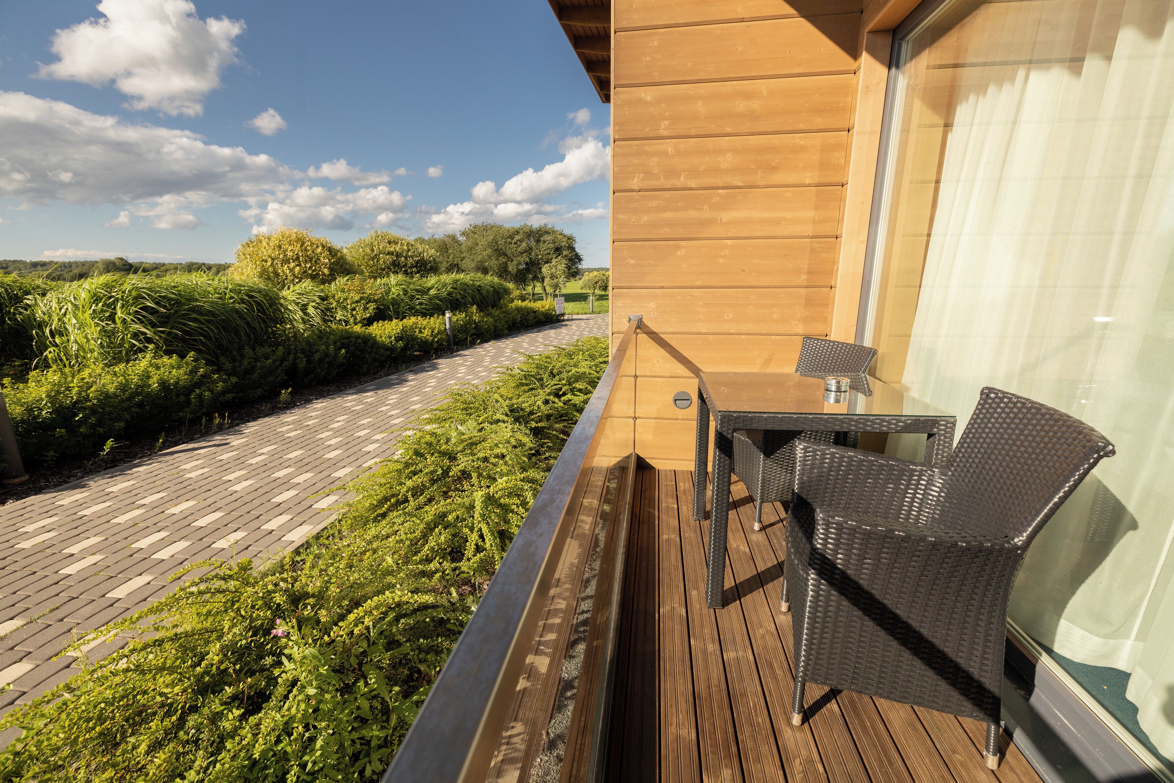 A wooden deck with a table and chairs, overlooking a landscaped garden and a clear sky.