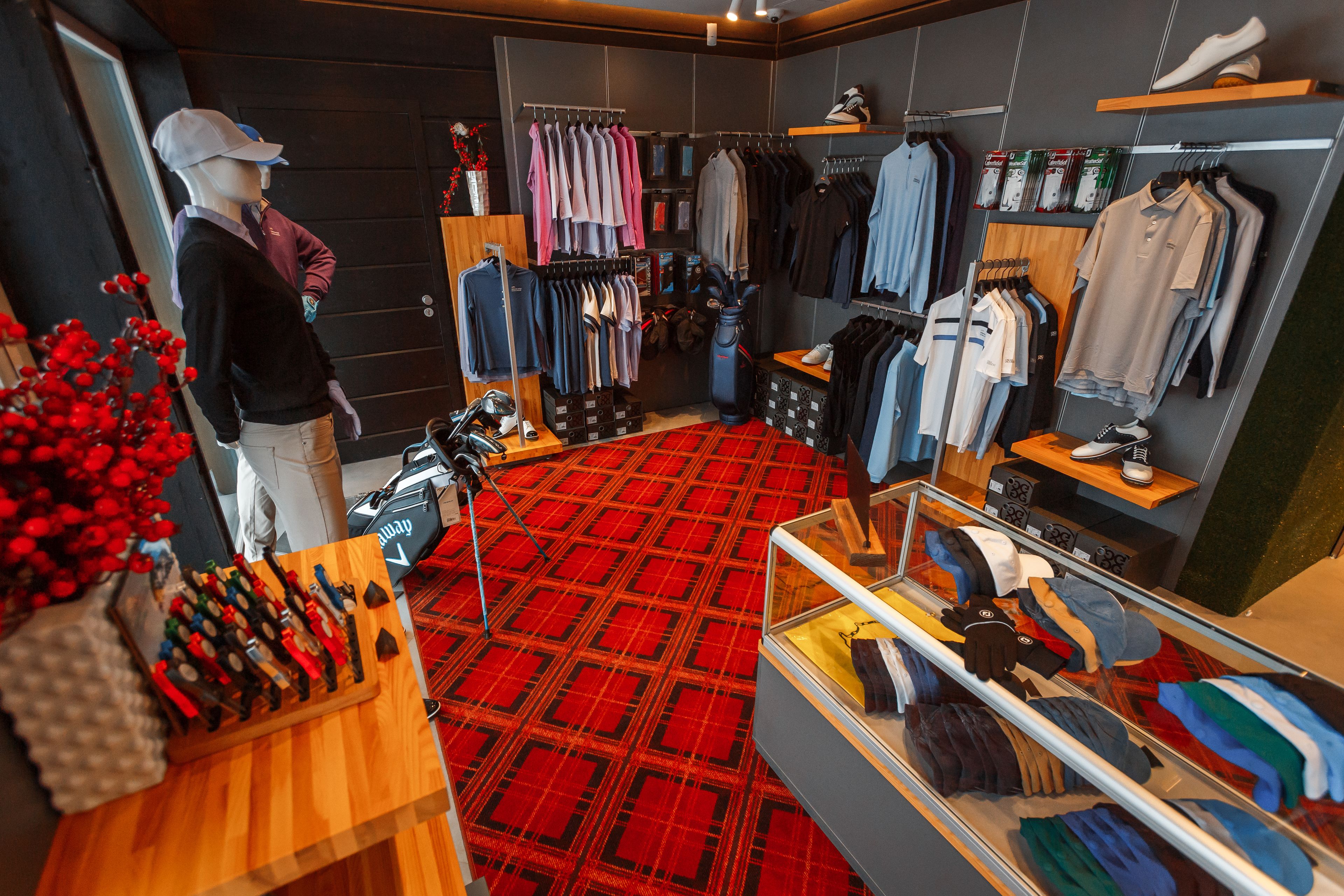 Una tienda de ropa con perchas llenas de camisas y pantalones, un maniquí y una exposición de guantes.