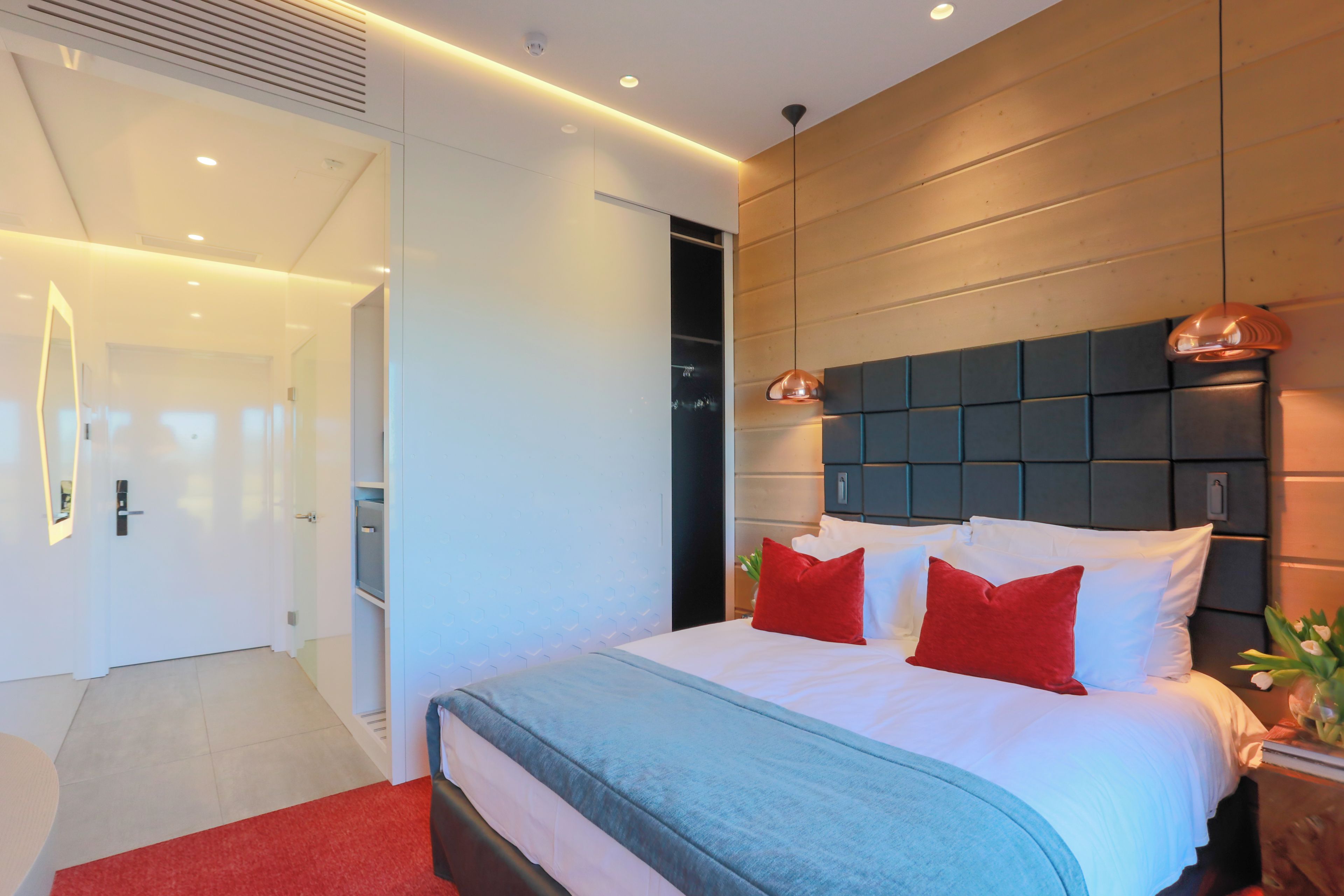 Un dormitorio moderno con una cama grande, un cabecero de madera y una almohada decorativa roja.