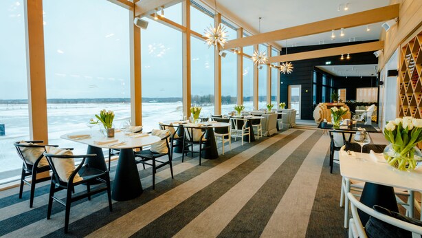 Een modern restaurant met grote ramen, een gestreept tapijt en gedekte tafels.