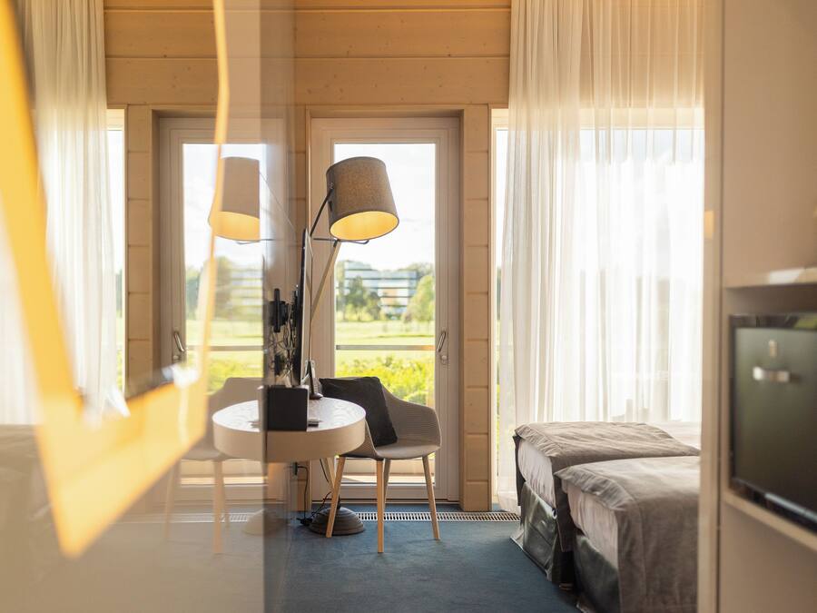Ett hotellrum med en säng, ett skrivbord med en stol, en lampa och en tv.