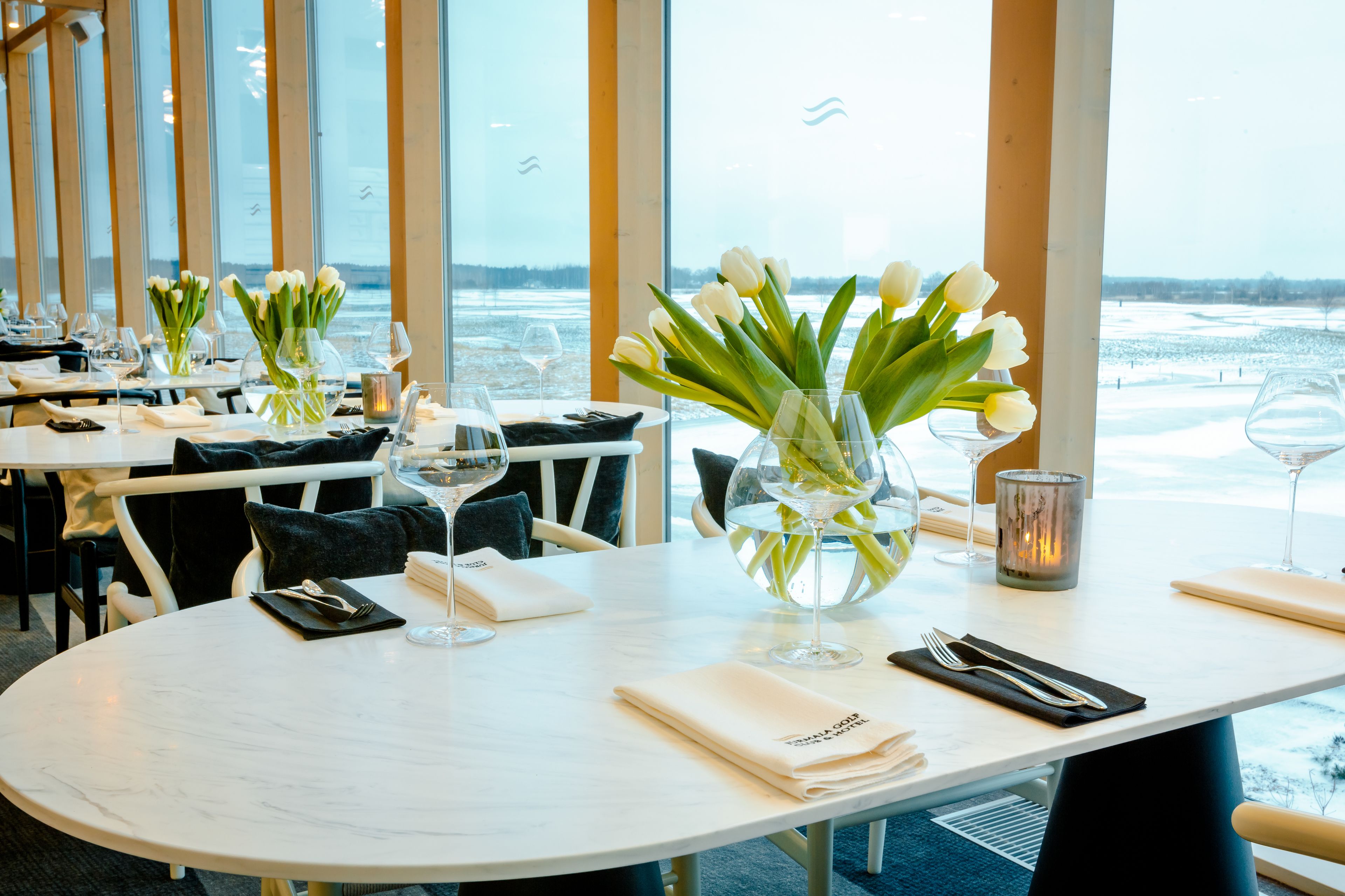 Een restaurant met gedekte tafels, tulpen in vazen, wijnglazen en uitzicht op de zee.
