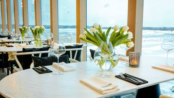 Een restaurant met gedekte tafels, tulpen in vazen, wijnglazen en uitzicht op de zee.
