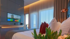 Een moderne hotelkamer met een groot bed, een aan de muur bevestigde televisie en uitzicht op de omgeving door grote ramen.