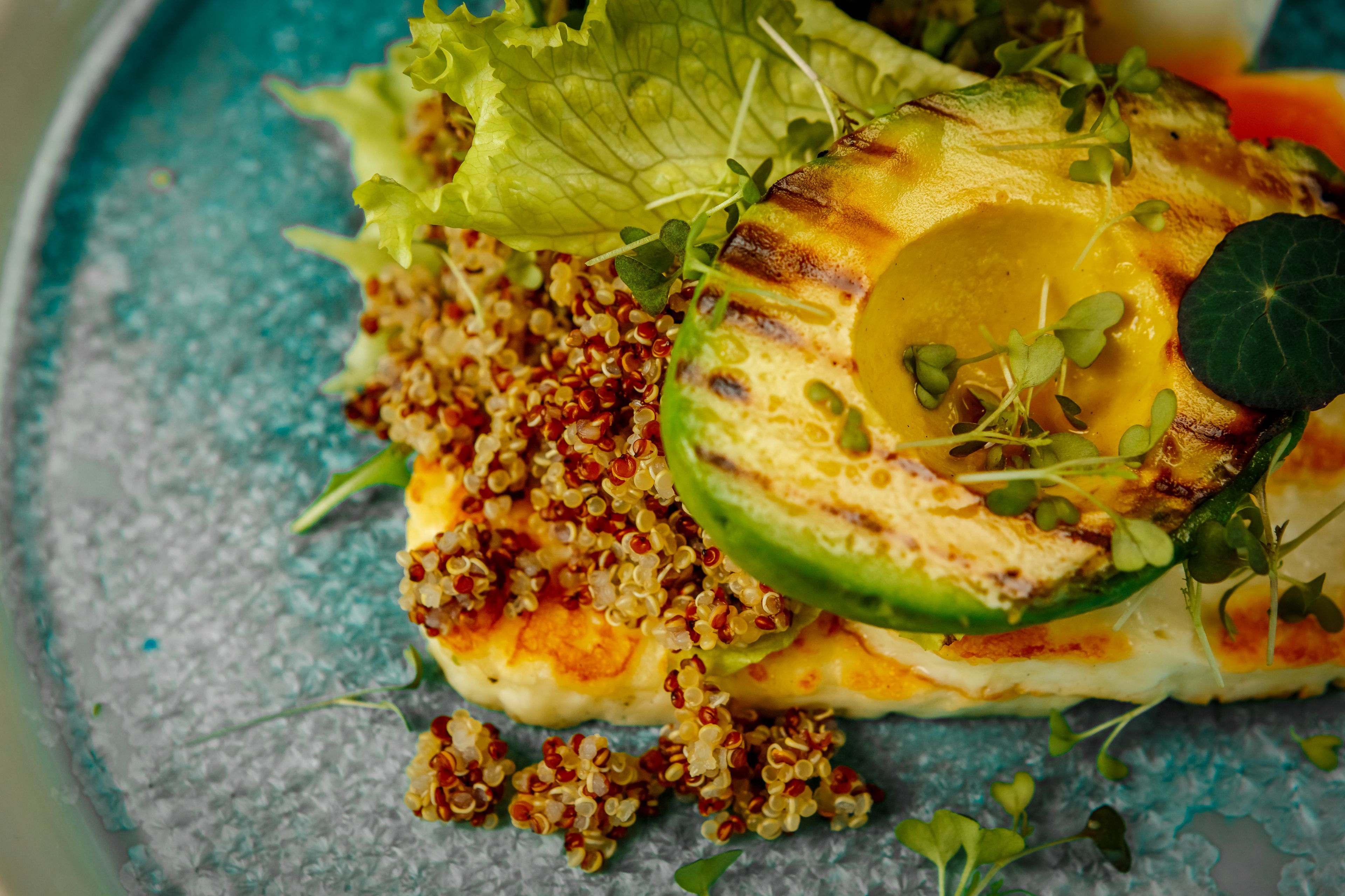 Primer plano de un plato con vegetales a la parrilla, quinoa y verduras sobre un plato azul con textura.