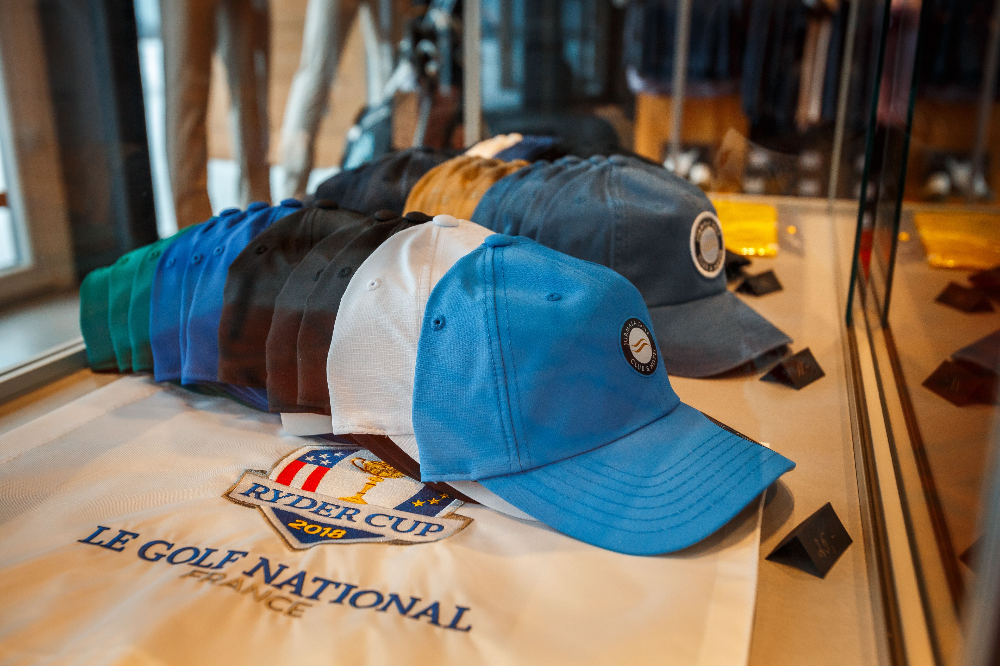 Exposição de bonés de golfe com um emblema da Ryder Cup 2019 e um letreiro 'Le Golf National'.