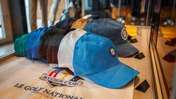Exposição de bonés de golfe com um emblema da Ryder Cup 2019 e um letreiro 'Le Golf National'.