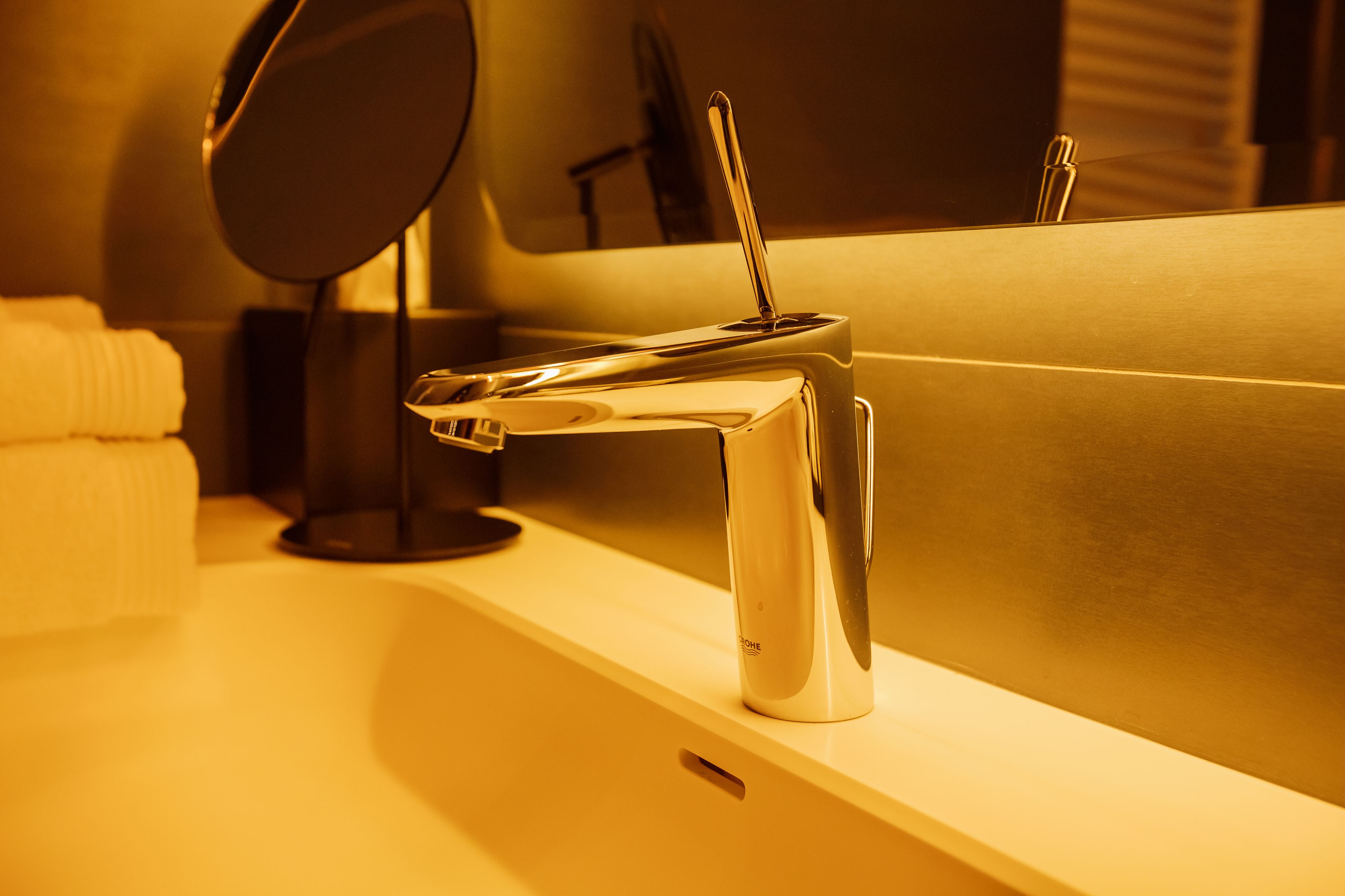 A modern bathroom with a chrome faucet, a mirror, and a towel on the counter.
