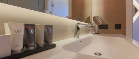 A modern bathroom with a large sink, a mirror, and toiletries on a shelf.