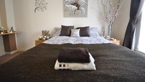 Een slaapkamer met een groot bed, twee nachtkastjes, een decoratief wandobject en een vaas met takken.