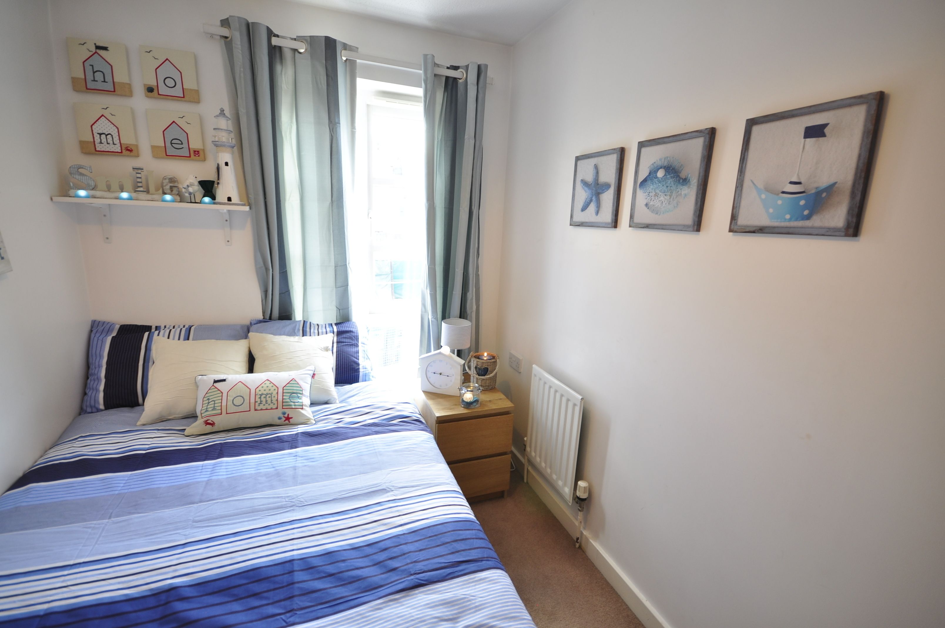 A bedroom with a bed, a nightstand, a shelf with decorative items, and a window with curtains.
