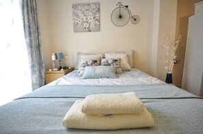 A neatly made bed with a bicycle-themed pillow, a wall-mounted bicycle decoration, and a vase with branches. - Durward Guest Apartment (London)