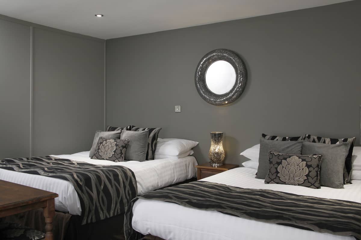 A hotel room with two beds, a round mirror on the wall, and a nightstand with a lamp.