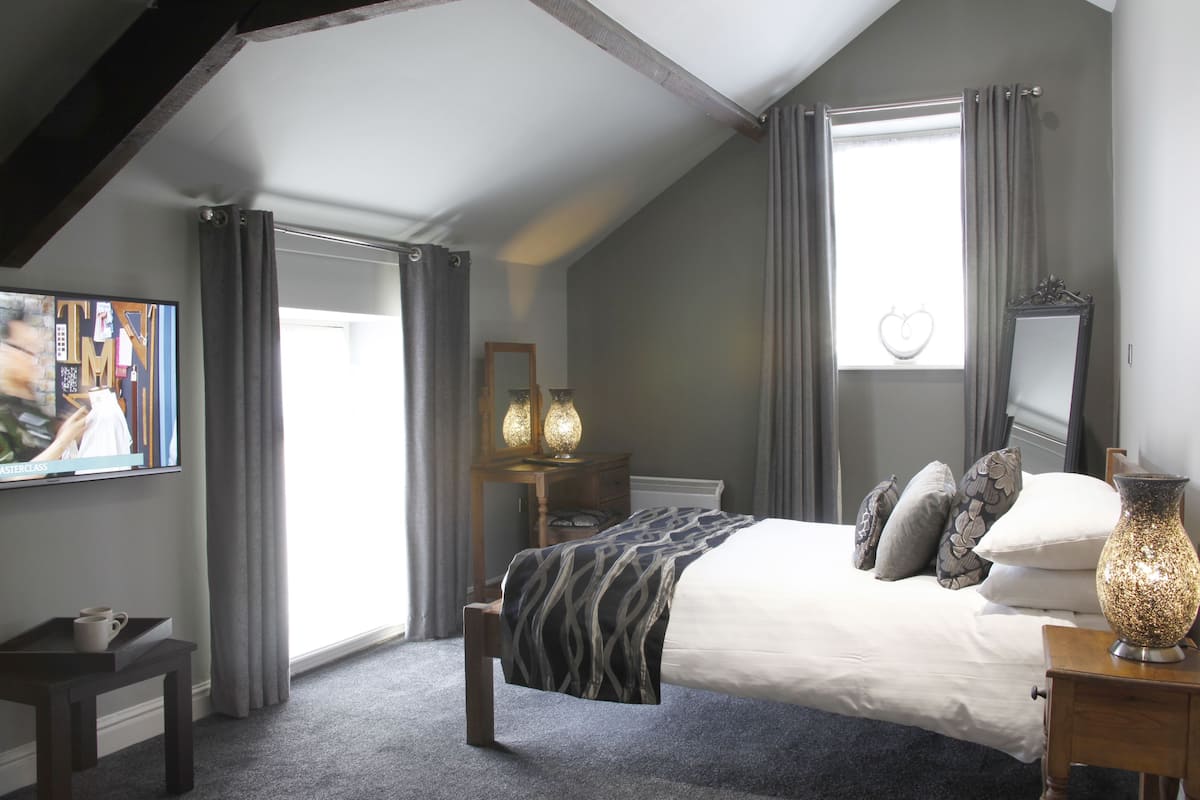 A bedroom with a large bed, a bedside table, a mirror, and a window with curtains.