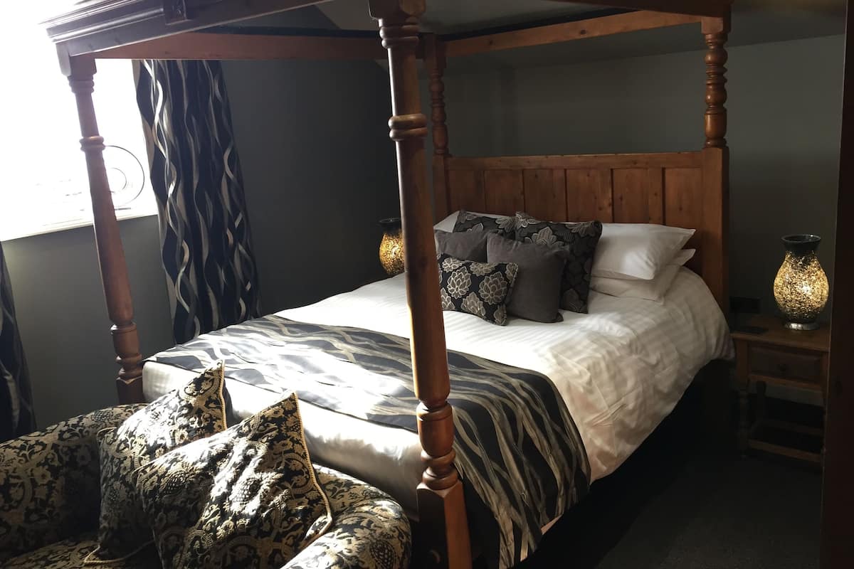 A four-poster bed with a wooden headboard, multiple pillows, and a bedside table with a lamp.