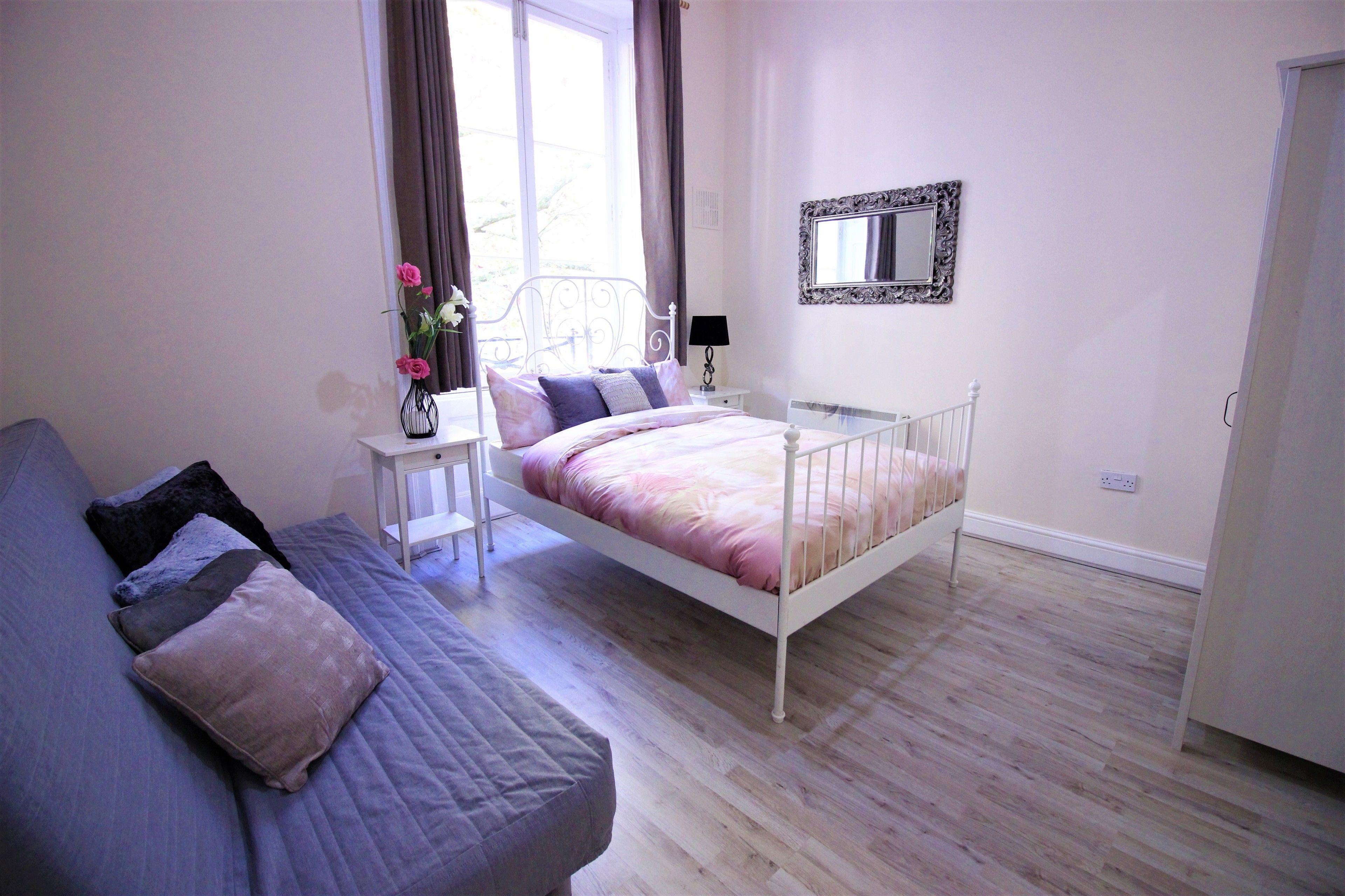 A bedroom with a bed, a bedside table with a lamp, a dresser, and a window with curtains.