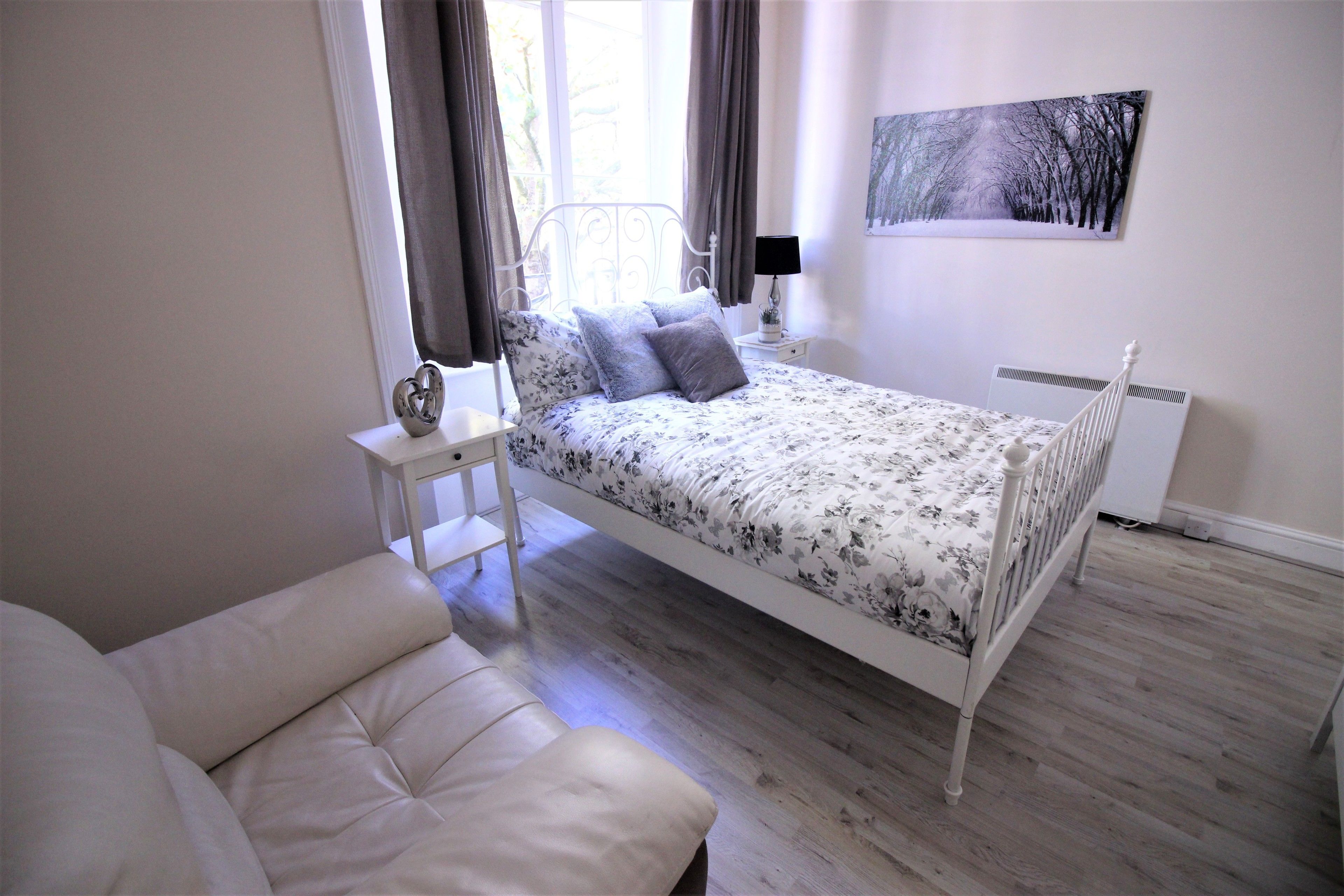 Un dormitorio con cama, mesita de noche, lámpara y un cuadro en la pared.