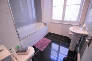 A bathroom with a bathtub, toilet, sink, and a window. - Paddington Guest Apartment (London)
