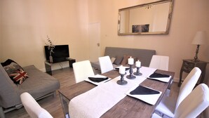 A dining area with a table set for four, a sofa with a Union Jack pillow, a television on a stand, and a mirror on the wall. - Paddington Guest Apartment (London)