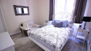 A bedroom with a white metal bed frame, a bedside table with a lamp, a nightstand, a chair, and a mirror on the wall. - Paddington Guest Apartment (London)