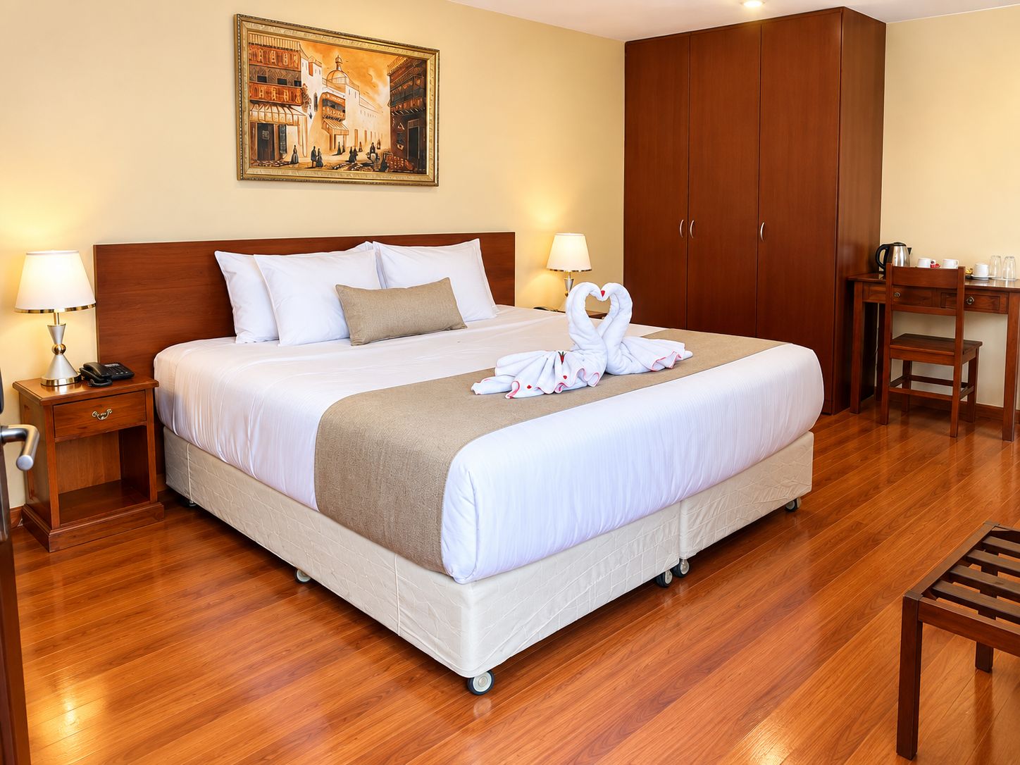 A hotel room with a king-sized bed, a desk, a chair, a nightstand, and a painting on the wall.