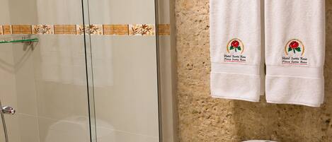Un baño con cabina de ducha de vidrio, un inodoro con la etiqueta 'INFECTA' y dos toallas colgadas en un perchero con la marca 'Hotel Santa Rosa'.