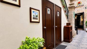 Un vestíbulo de hotel con una jardinera de madera, dos puertas señalizadas para hombres y mujeres, una escalera y un cuadro en la pared.
