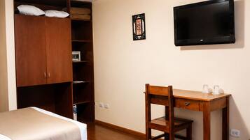 A hotel room with two beds, a desk, a television, a wardrobe, and a ceiling light.