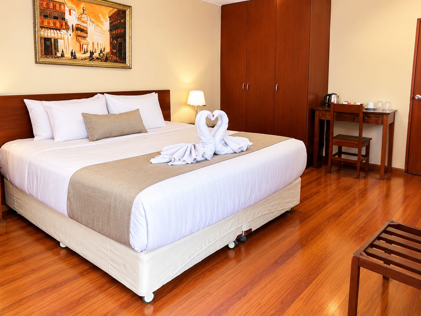Quarto de hotel com uma cama grande, uma escrivaninha, uma cadeira e um quadro na parede.