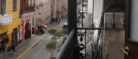 A balcony overlooking a street with buildings, a church, and a red flag.